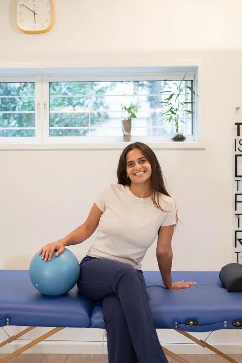 גל עופרי פיזיותרפיסטית מוסמכת יושבת על מיטת הטיפולים בקליניקה ומחייכת